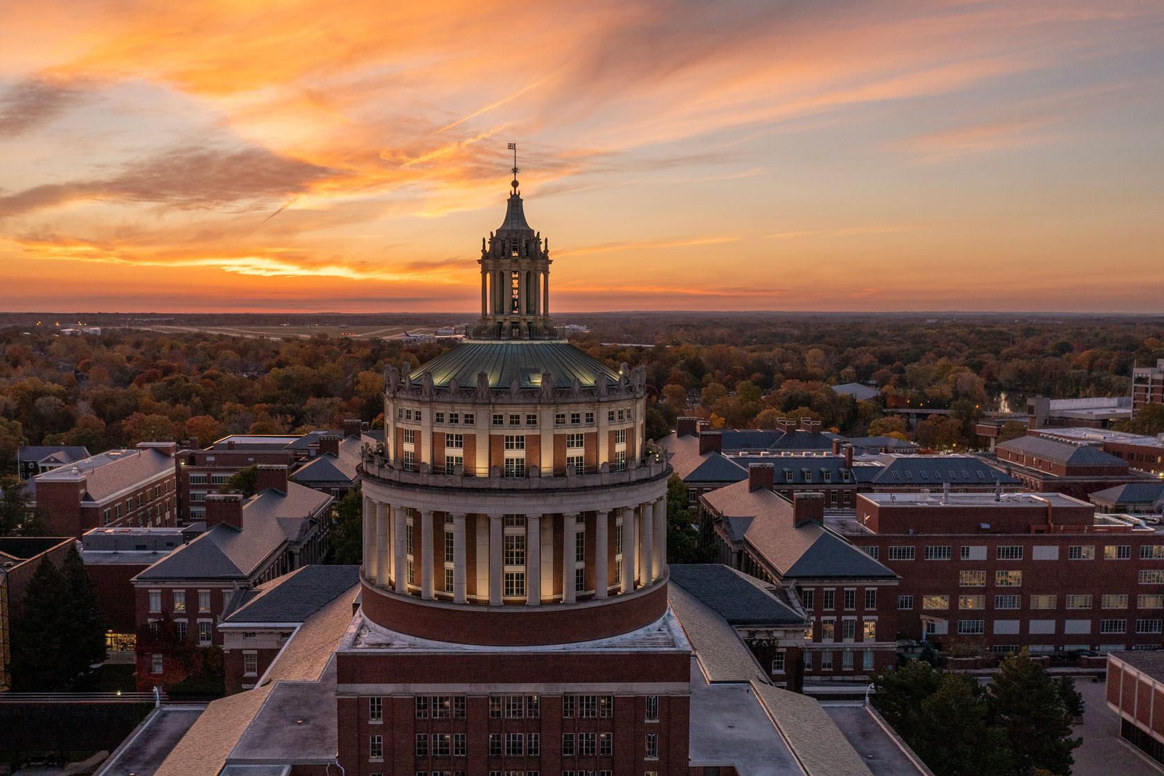 The sun sets behind the University of Rochester, casting a warm glow over the campus building.